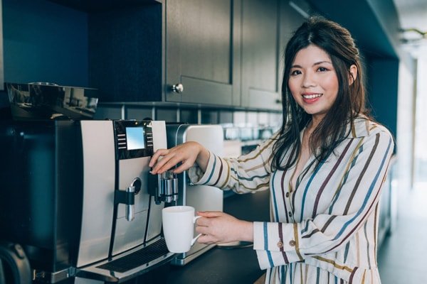 A woman using a cofeee dispenser to get fresh coffee, leading breakroom services management company